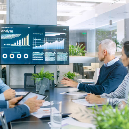 Board of Directors Has Annual Meeting, Diverse Group of Business People in the Modern Conference Room Discuss Statistics and Work Results. In the Background Projector Showing Company Growth.