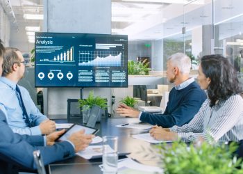 Board of Directors Has Annual Meeting, Diverse Group of Business People in the Modern Conference Room Discuss Statistics and Work Results. In the Background Projector Showing Company Growth.